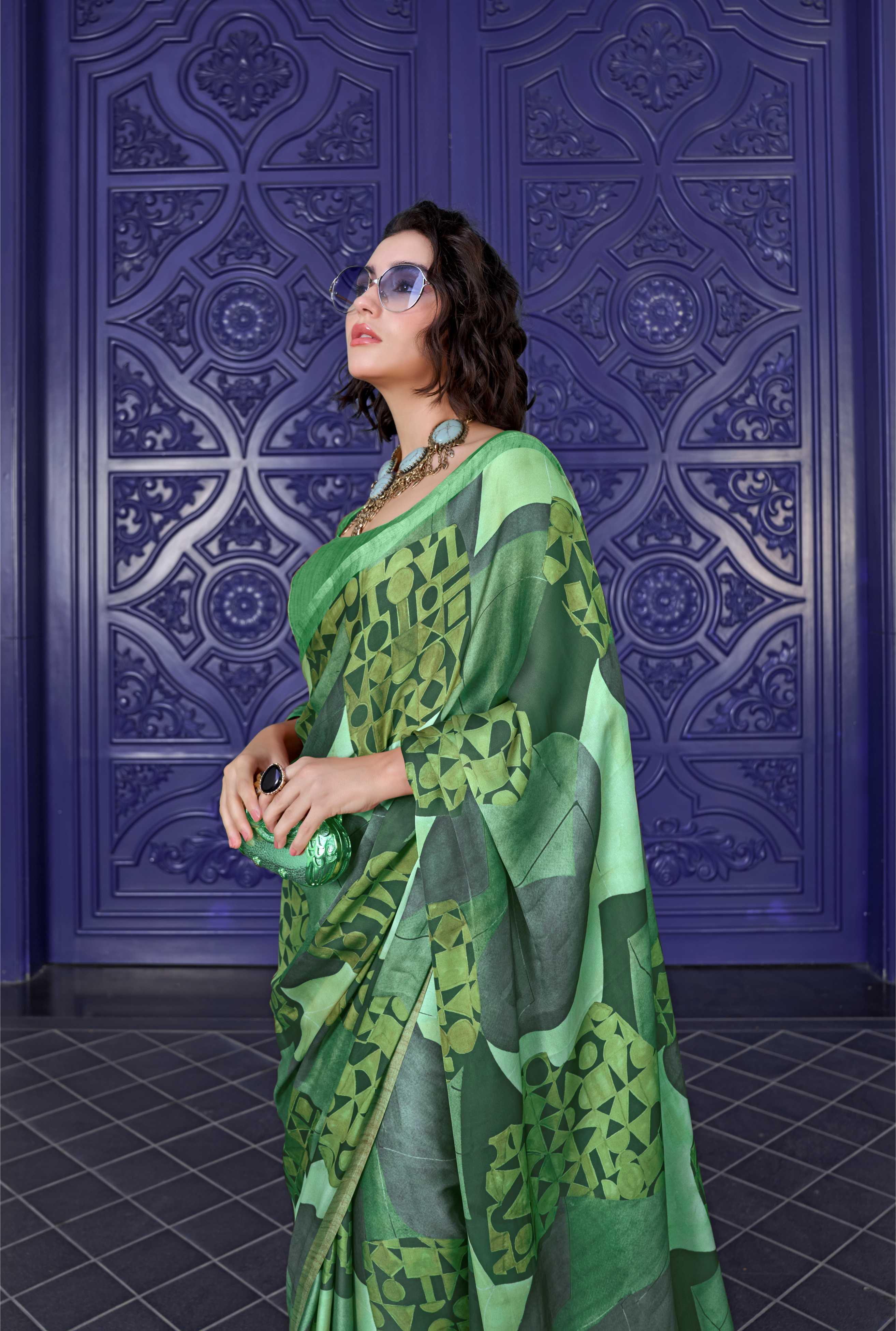 Woman wearing a green saree with a pattern against a decorative purple wall.