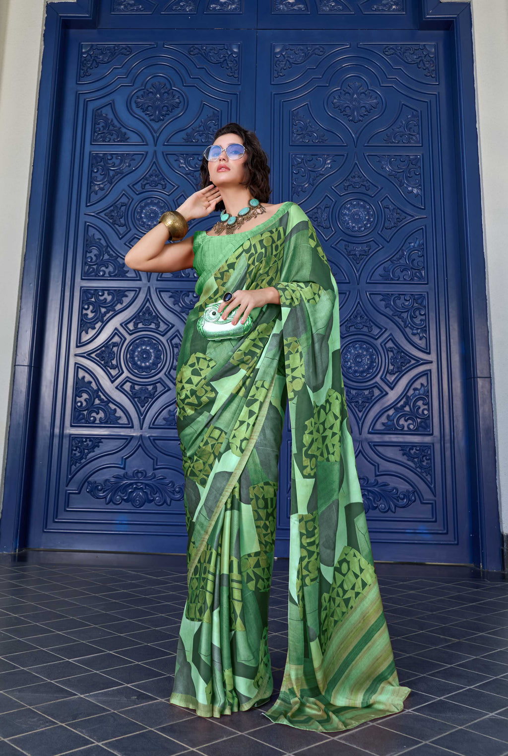 Woman in a green saree standing in front of a blue decorative door.