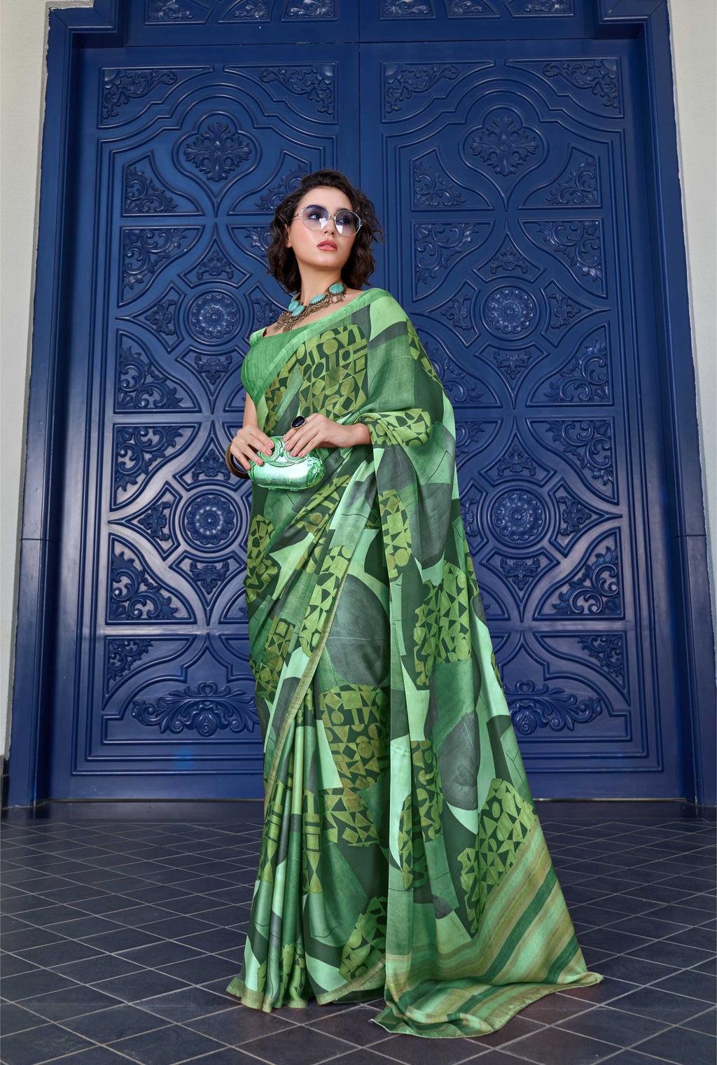 Woman in a green saree standing in front of a blue ornate door.