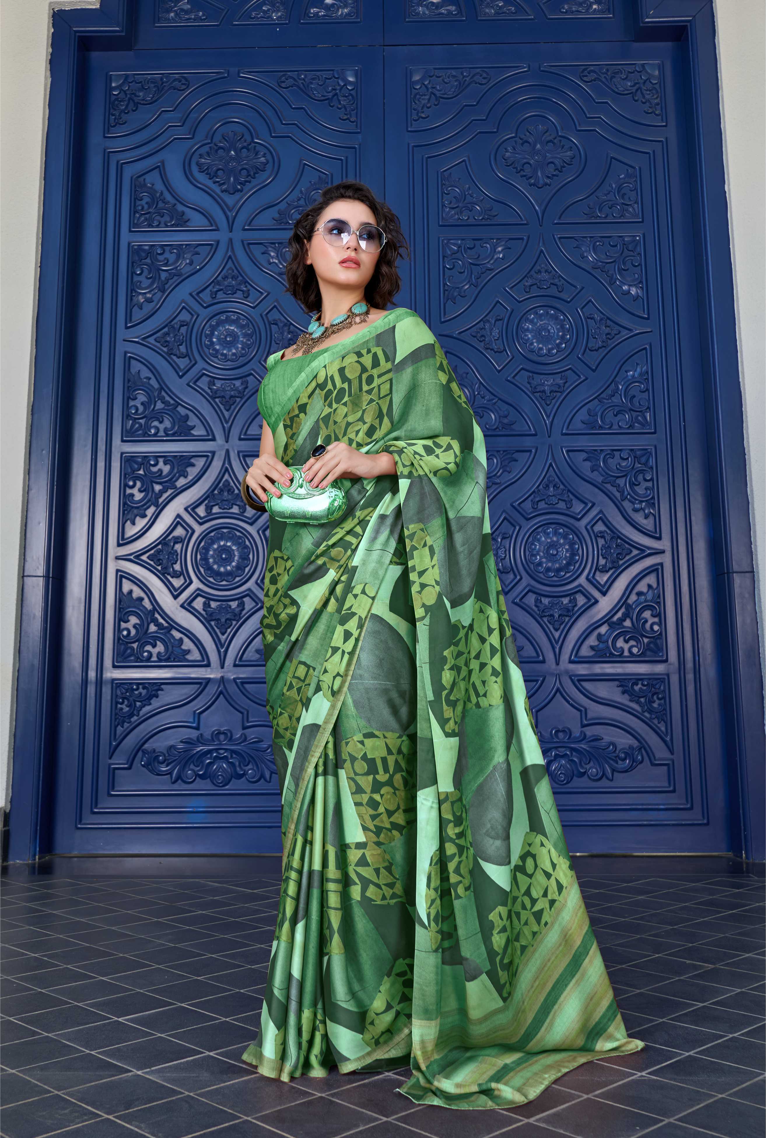 Woman in a green saree standing in front of a blue ornate door.